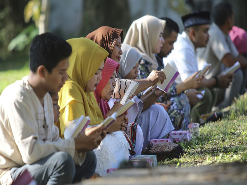 Personas leen el Corán mientras oran en el lugar en donde está una fosa común con las víctimas del tsunami (AP Foto/Nurhasanah)